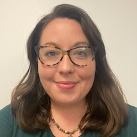 Woman with long brown hair, tortoise shell glasses, and a green shirt
