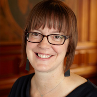 A woman with short brown hair and glasses in a black shirt.